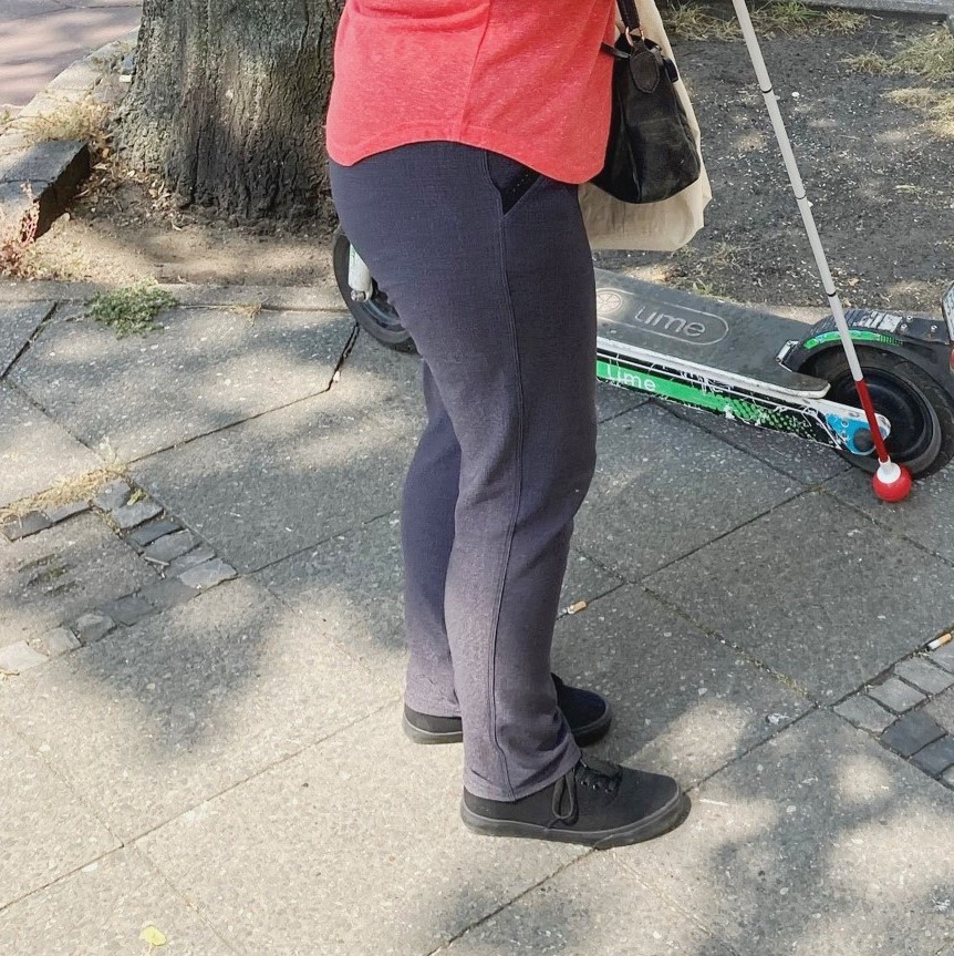 Farbfoto: Ein auf dem Gehweg stehender E-Roller versperrt einer Person mit Blindenlangstock den Weg.