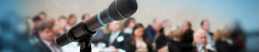 Nahaufnahme Mikrofon, im Hintergrund Zuschauer